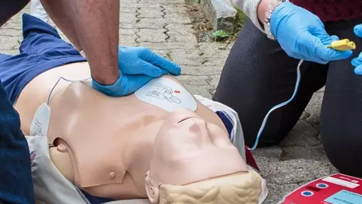 Due soccorritori che applicano un defibrillatore su un manichino d'esercitazione, durante una sessione di addestramento per la rianimazione cardiopolmonare (RCP). L'immagine rappresenta l'importanza dell'addestramento e della preparazione degli operatori sanitari per fronteggiare situazioni di emergenza, in particolare quelle relative a problemi cardiaci. L'applicazione del defibrillatore sul manichino indica la prontezza ad agire e l'importanza delle tecniche di RCP per salvare vite umane in caso di arresto cardiaco.